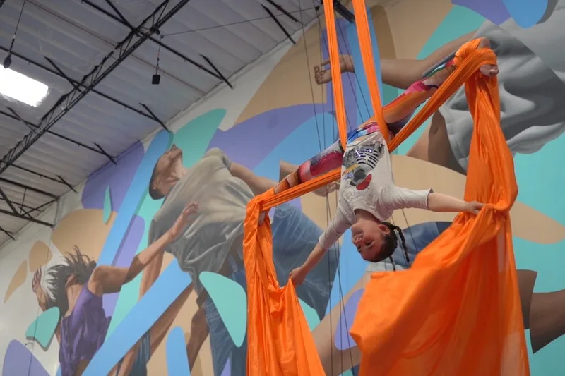 An aerial student practicing on orange silks inside the colorful LVCC training space